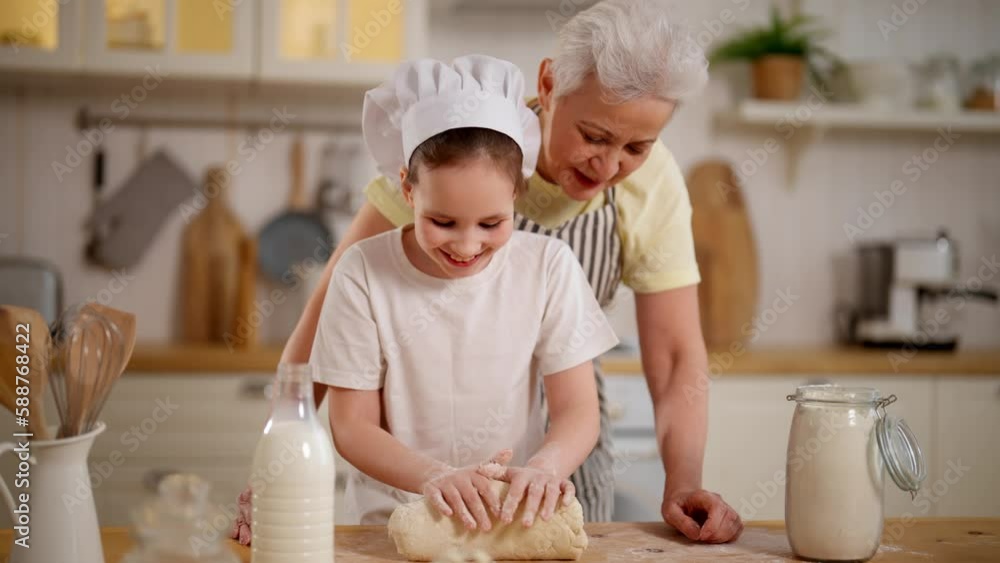 Happy granny explaining granddaughter knead dough in kitchen at home