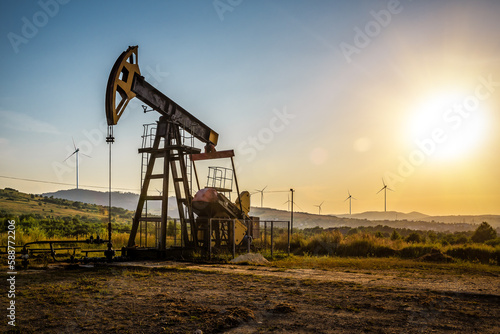 Oil pump and wind turbines at sunset