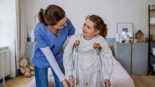 Photo Young nurse helping to walk to little girl with broken leg.