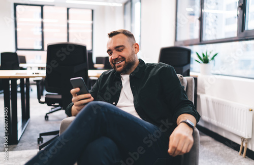Happy male entrepreneur surfing internet on smartphone in office