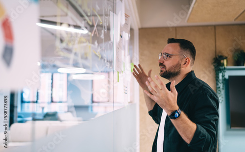 Frustrated male economist having business problem working with calculations on glass wall