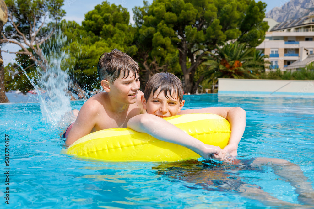 Two kids boys having fun on inflatable rubber rings in outdoor pool. Summer holiday. Summertime kids weekend. Children having fun, brothers on family vacations. Two kids boys having fun on inflatable rubber rings in outdoor pool. Summer holiday. Summertime kids weekend. Children having fun, brothers on family vacations.