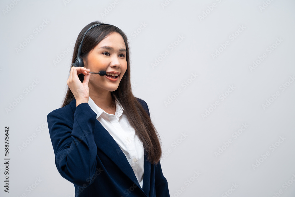Beautiful Asian call center operator talking with customer using headset and microphone isolated on grey background. Beautiful Asian call center operator talking with customer using headset and microphone isolated on grey background.