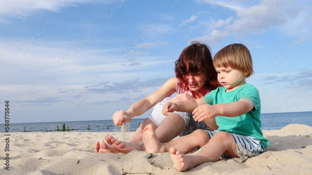 Mother playing with little child boy on sand beach. Adult woman and her son enjoying summer day on seshore. Family holiday at sea. Slow motion Mother playing with little child boy on sand beach. Adult woman and her son enjoying summer day on seshore. Family holiday at sea. Slow motion