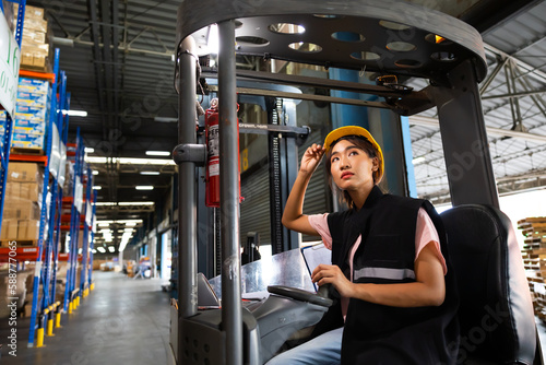 Asian female warehouse worker drive forklift in warehouse. Warehouse staff worker by goods shelf working in large warehouse factory © NVB Stocker
