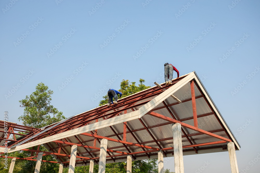 Roof repair, Construction worker installing new roof, roofing tools, power drill used on new roof with sheet metal. Roofing - construction worker standing on a roof covering it with metal.