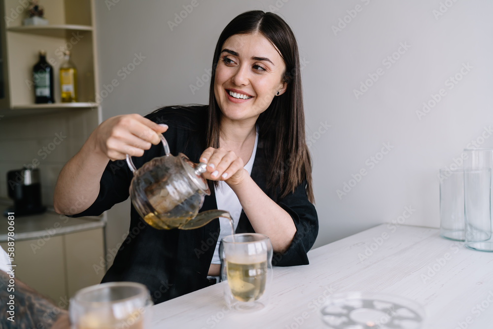 Smiling woman pouring tea into cup from pot Smiling woman pouring tea into cup from pot