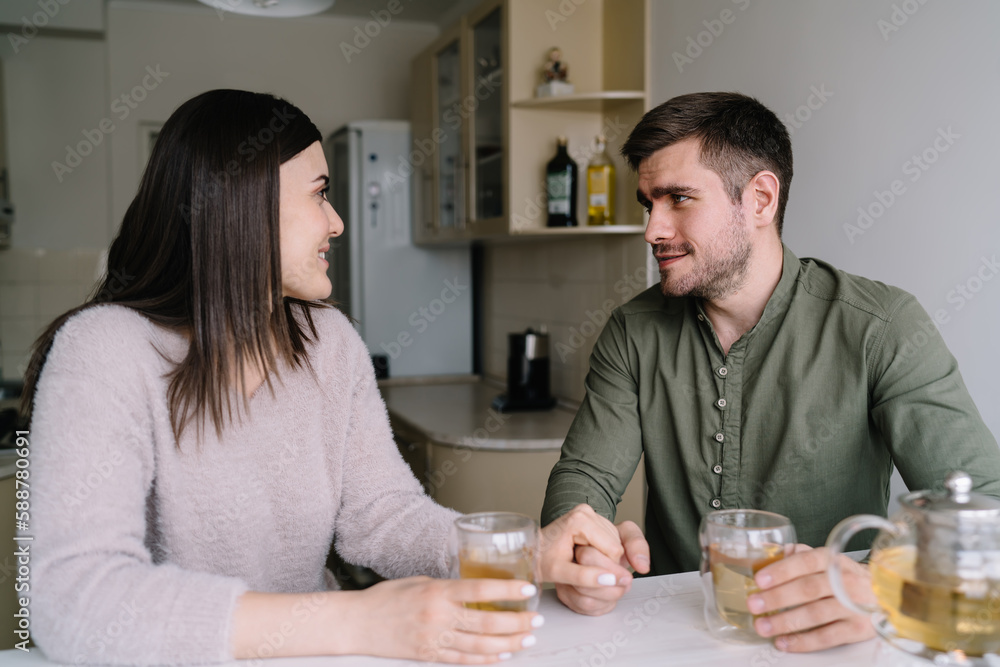 Happy couple sitting at table and drinking tea in kitchen Happy couple sitting at table and drinking tea in kitchen