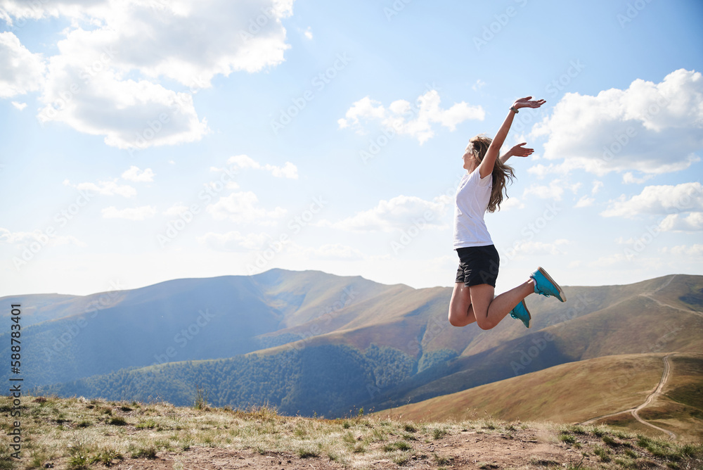 Young woman jumping on top of the mountain. Feeling happy and free. Natural landscape in summer. Sunny rural scenery. Nature protection concept. Breathtaking mountain view.. On top of the world Young woman jumping on top of the mountain. Feeling happy and free. Natural landscape in summer. Sunny rural scenery. Nature protection concept. Breathtaking mountain view.. On top of the world