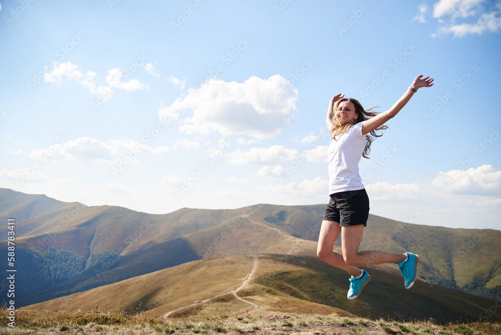 Young woman jumping on top of the mountain. Feeling happy and free. Natural landscape in summer. Sunny rural scenery. Nature protection concept. Breathtaking mountain view.. On top of the world Young woman jumping on top of the mountain. Feeling happy and free. Natural landscape in summer. Sunny rural scenery. Nature protection concept. Breathtaking mountain view.. On top of the world