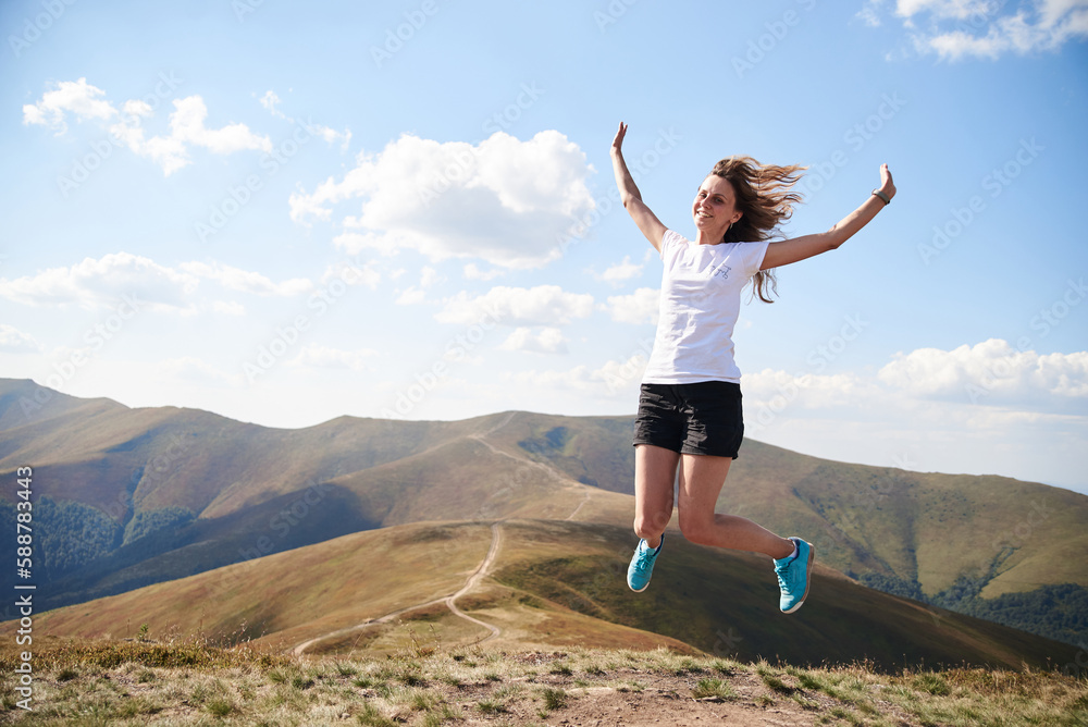 Young woman jumping on top of the mountain. Feeling happy and free. Natural landscape in summer. Sunny rural scenery. Nature protection concept. Breathtaking mountain view.. On top of the world Young woman jumping on top of the mountain. Feeling happy and free. Natural landscape in summer. Sunny rural scenery. Nature protection concept. Breathtaking mountain view.. On top of the world