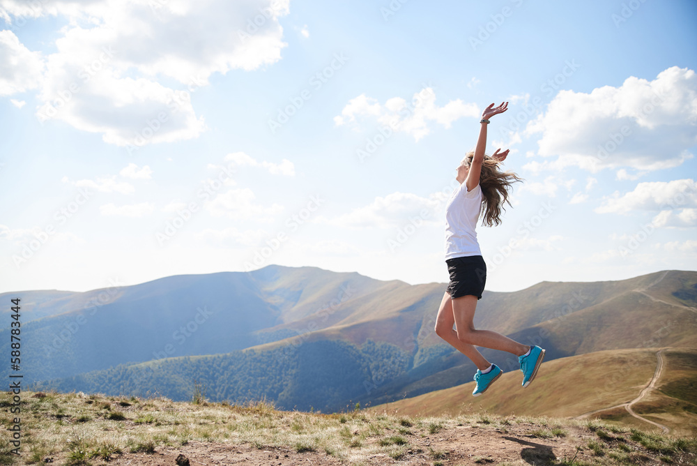 Young woman jumping on top of the mountain. Feeling happy and free. Natural landscape in summer. Sunny rural scenery. Nature protection concept. Breathtaking mountain view.. On top of the world