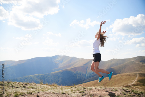Young woman jumping on top of the mountain. Feeling happy and free. Natural landscape in summer. Sunny rural scenery. Nature protection concept. Breathtaking mountain view.. On top of the world