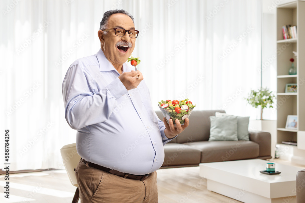 Mature man standing and eating a salad in a living room Mature man standing and eating a salad in a living room