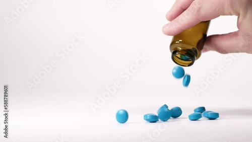 Blue pills falling out from a traditional pharmacy bottle. Treatment and prevention of diseases. Male hand holding a brown bottle. Assortment of medicinal pharmaceutical products with white background photo