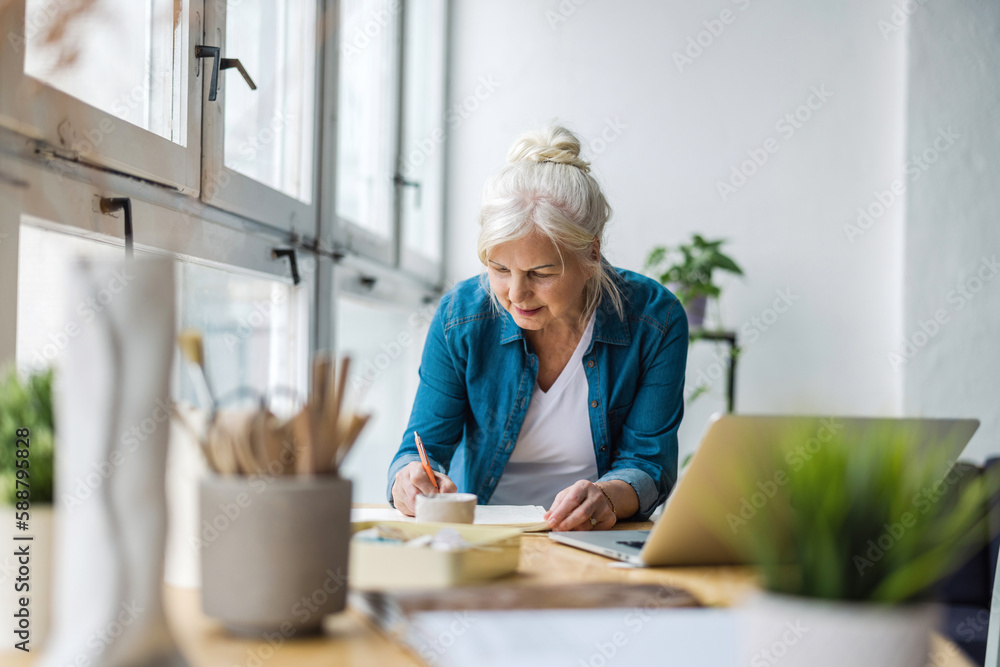 Smiling mature businesswoman writing in notebook while sitting at table in office Smiling mature businesswoman writing in notebook while sitting at table in office