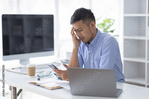 Happy caucasian young Asian man using smart phone cellphone for calls, social media, mobile application online in office money financial planning concept