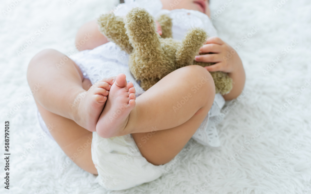 Selective focus legs of little baby girl, laying, sleeping on white comfortable bed in cozy indoor home with copy space. Kid Development Concept. Selective focus legs of little baby girl, laying, sleeping on white comfortable bed in cozy indoor home with copy space. Kid Development Concept.