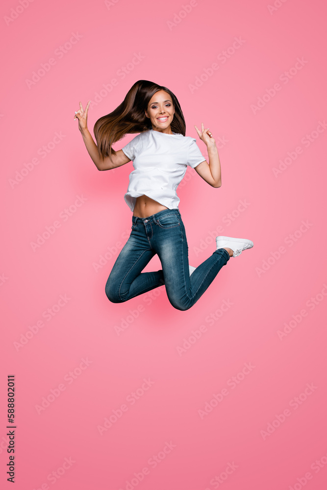 Concept of carefree life. Full-body full-size portrait of happy jumps girl which shows v-sign isolated on gray background Concept of carefree life. Full-body full-size portrait of happy jumps girl which shows v-sign isolated on gray background