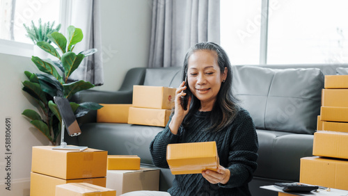 Successful asia people woman entrepreneur with parcel boxes checking email order in tablet and laptop at sofa home office SMEs small company.