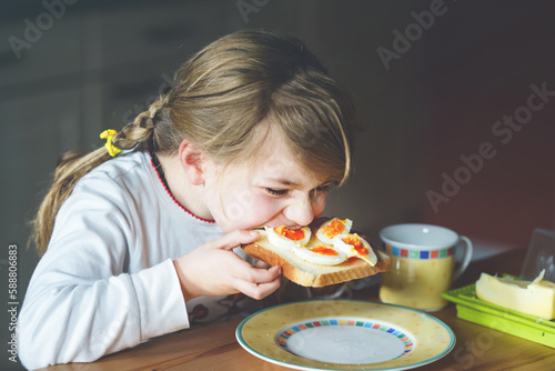 Little smiling girl have a breakfast at home. Preschool child eating sandwich with boiled eggs. Happy children, healthy food and meal.