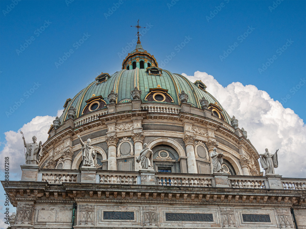 Copenhagen, Denmark - September 13, 2010: Back side, outside apse, view on beige stone Frederiks church with green dome under blue cloudscape. Row of 4 stone statues 