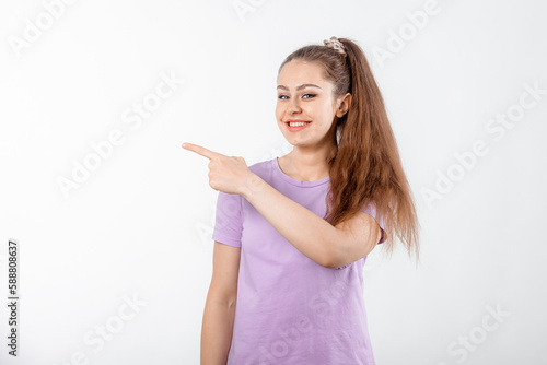 Wallpaper Mural Enthusiastic young woman with long hair, pointing finger left and look happy, showing great promo offer aside, standing in casual t shirt over white background Torontodigital.ca