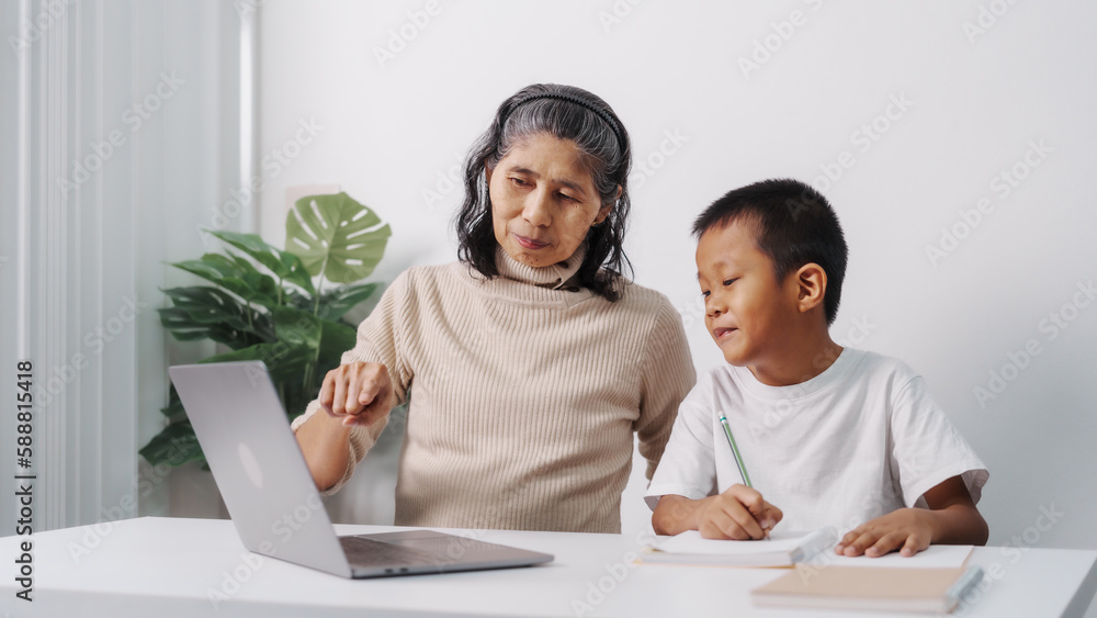 Learning online maths class on laptop computer pc, Asian grandson and grandmother people sitting together at desk doing homework at home. Learning online maths class on laptop computer pc, Asian grandson and grandmother people sitting together at desk doing homework at home.