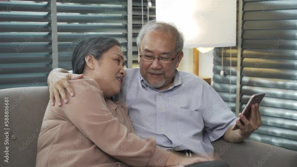 An elderly Asian couple, about 60 years old, in the living room. Are using smartphone video calls to talk to family members with joy and happiness. An elderly Asian couple, about 60 years old, in the living room. Are using smartphone video calls to talk to family members with joy and happiness.