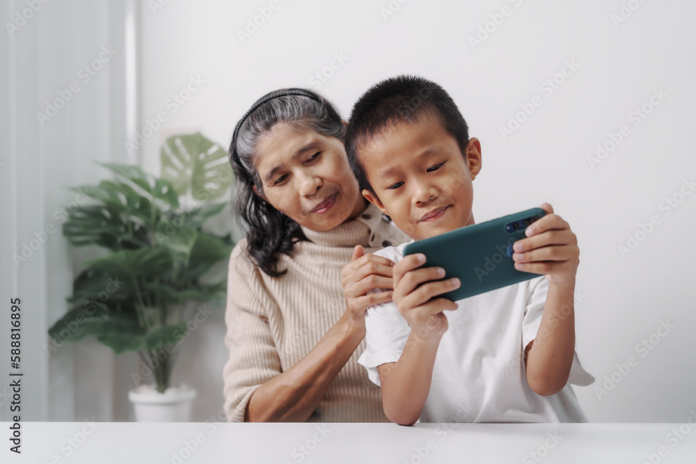 Playing mobile game together, Asian grandson and grandmother people sitting together at desk. Playing mobile game together, Asian grandson and grandmother people sitting together at desk.