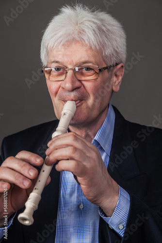 Portrait of an elderly musician in glasses and a dark suit playing a pipe. 