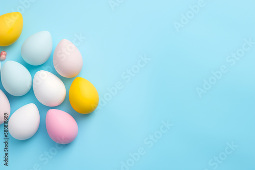 Conceito de festa de Páscoa. Foto de vista superior de orelhas de coelhinho da páscoa ovos azuis rosa e amarelos em fundo azul pastel isolado com copyspace no meio