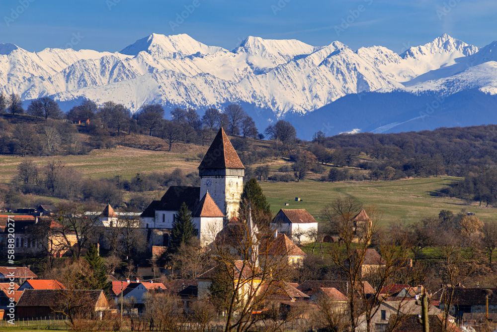 Photography of the fortified church located at Hosman, Sibiu county, Romania shot in the mid day with the Fagaras  mountains in the background.