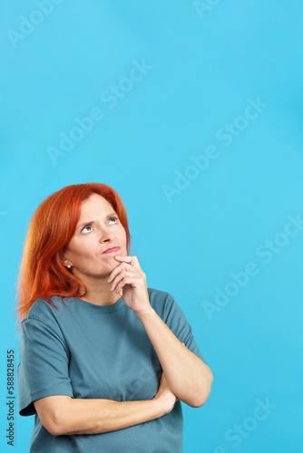 Redheaded mature woman with hand on face and thoughtful expression