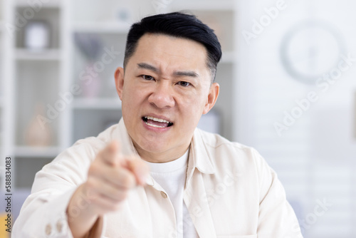 Video call online meeting, mature adult asian looking at camera angry man shouting angry, businessman working remotely from home talking to colleagues, boss nervous at home talking to subordinates.