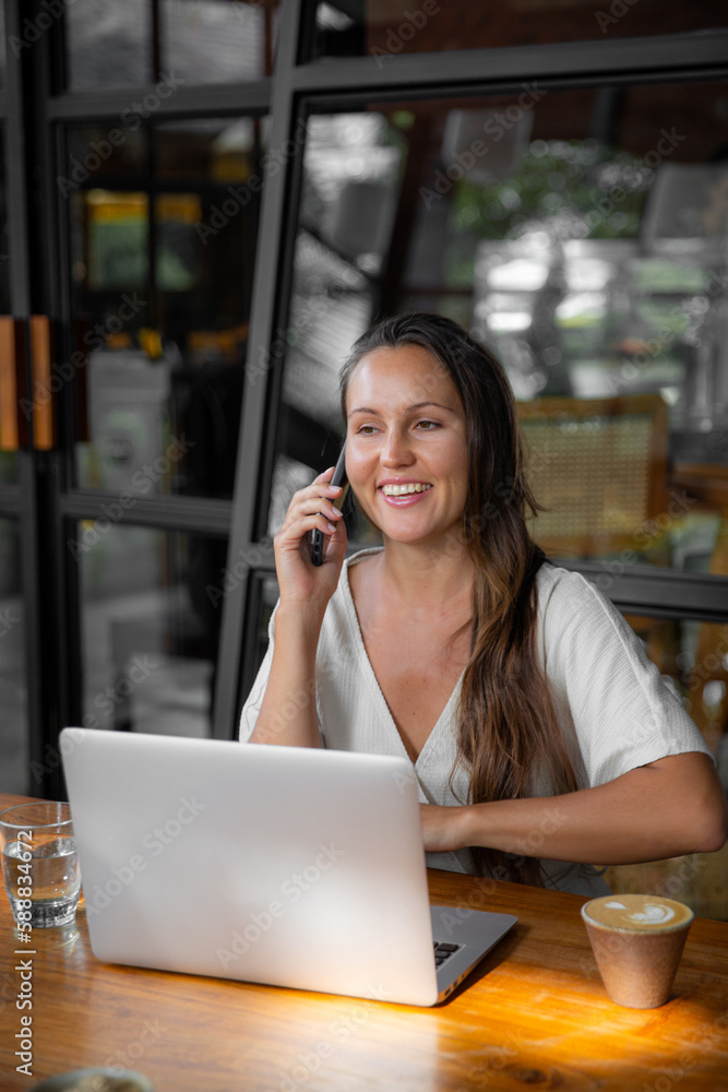 Happy long haired woman in casual clothing using laptop and talking by phone. Happy long haired woman in casual clothing using laptop and talking by phone.