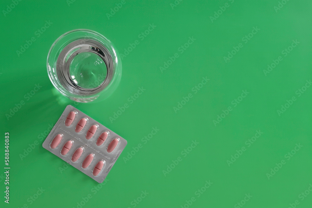 Tablets and glass of water. Flat lay. Place for text. Pills in package and water on green background. Vitamins and medicines. Concept of health, treatment, disease prevention. Copy space. Top view.