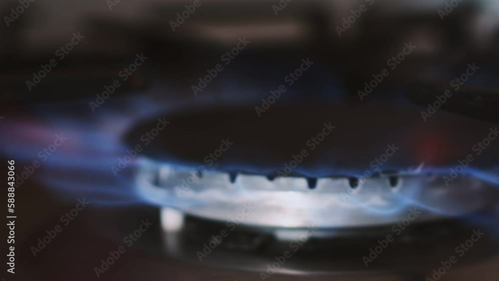 Closeup of gas burner on stove at kitchen that is lit by blue flame, side view. Gas burner spontaneously ignites with blue flame. Concept of gas and energy crisis Closeup of gas burner on stove at kitchen that is lit by blue flame, side view. Gas burner spontaneously ignites with blue flame. Concept of gas and energy crisis