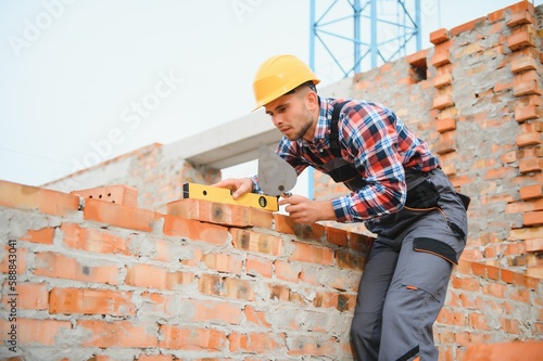 construction mason worker bricklayer installing red brick with trowel putty knife outdoors.