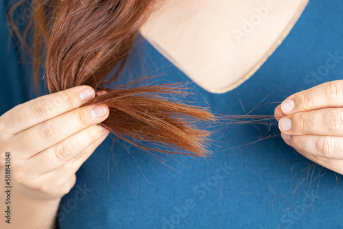 Unrecognizable long red haired woman in blue shirt holding bundle of hair in hand and turning one hair item on white background. Hair loss and alopecia problem. healthcare and skin treatment