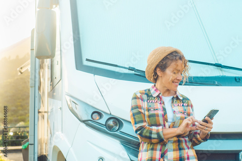 Woman driver enjoy camper parking rv area using phone app to plan next destination of travel. Happy tourist with van vehicle and roaming connection mobile technology. Traveler motor home lifestyle