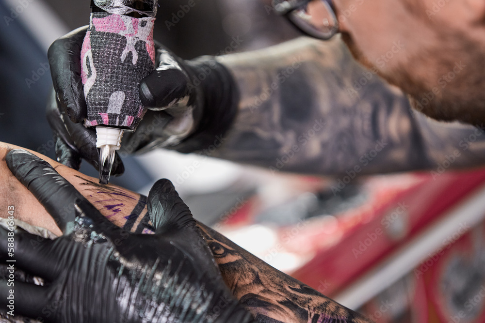 Close up tattoo machine. Tattooing. Man creating picture on his arm by a professional tattoo artist.