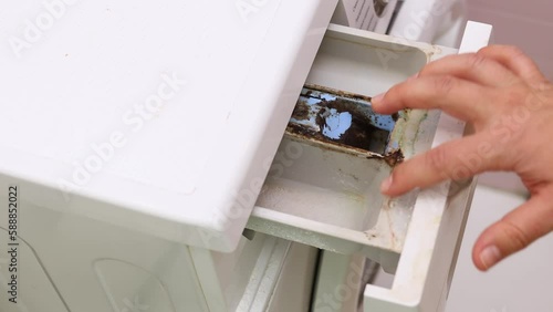 Open washing machine drawer of powder container, top view closeup. Touch with hand dark clumps of dirt and mold inside. Dirty washer container. Uncleaned household appliances, untidy house.