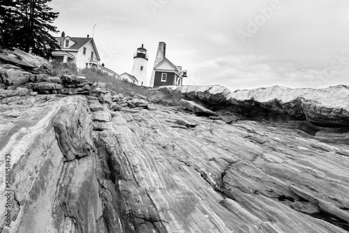 Pemaquid Point Lighthouse, Maine. View of Lighthouse and keeper's house from the bottom of rocky cliff looking upwards towards lighthouse sitting on top of the promontory. Black and white.