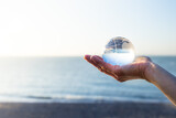 Crystal Earth globe in hand in front of the sea and beach at sunset. Environment and ocean care concept. Glass ball globe in nature. Earth care symbol