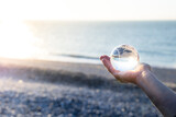 Crystal Earth globe in hand in front of the sea and beach at sunset. Environment and ocean care concept. Glass ball globe in nature. Earth care symbol