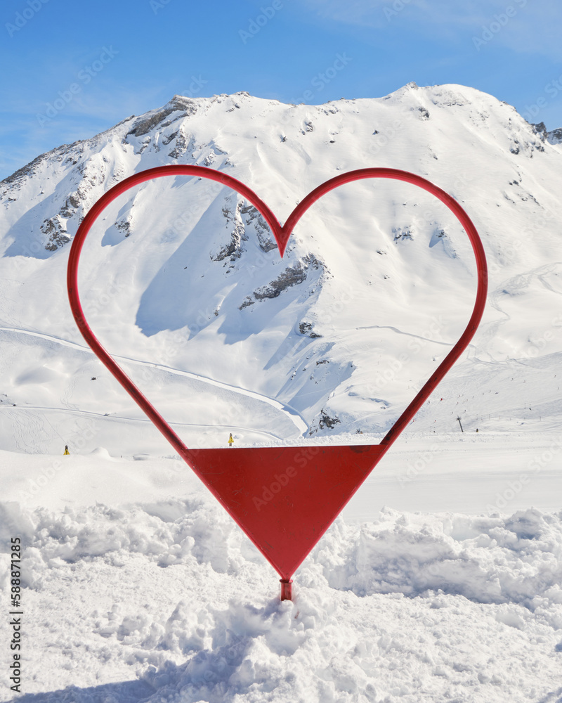 Photo frame shaped like a red heart in Val d'Isere ski resort, France, in Winter, used for tourists to take photos with the slopes and mountains in the background.