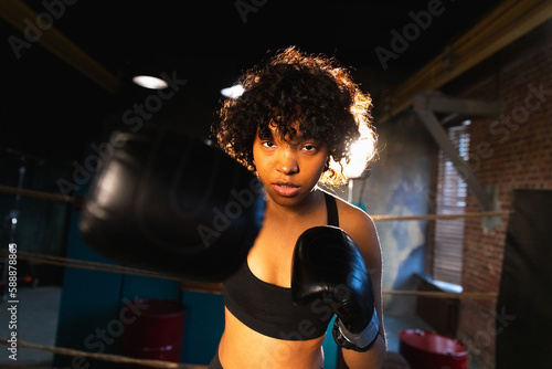 Women self defense girl power. African american woman fighter punching with boxing gloves to camera. Healthy strong girl punching training punches looking concentrated straight. Fit body workout © Юлия Завалишина