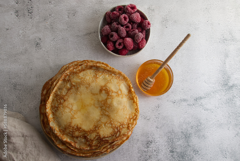Stack of fresh crepes with honey and raspberries on the table copy space