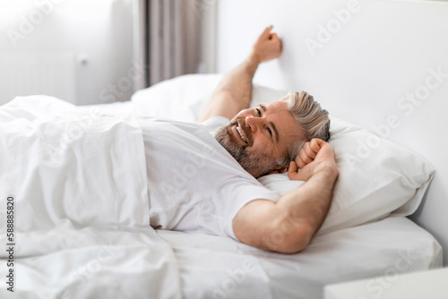 Positive mature man stretching in bed in the morning